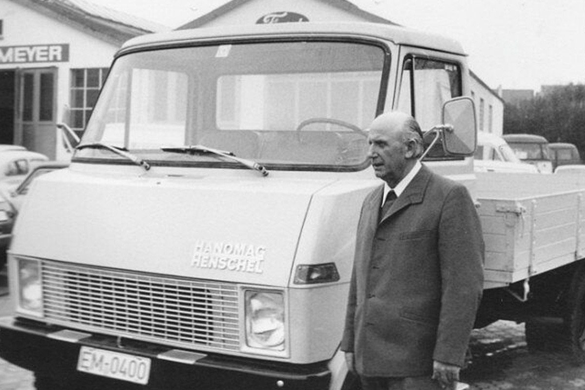 Ein schwarz-weißes Foto mit einem Mann und einem Auto vor dem Auto-Meyer Schild